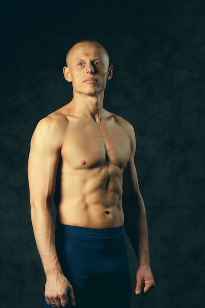 Foto gespierde model sport jonge man op donkere achtergrond. mode portret van sterke brute man met een moderne trendy kapsel. sexy romp. mannetje dat zijn spieren buigt. sport training bodybuilding concep. afgezwakt