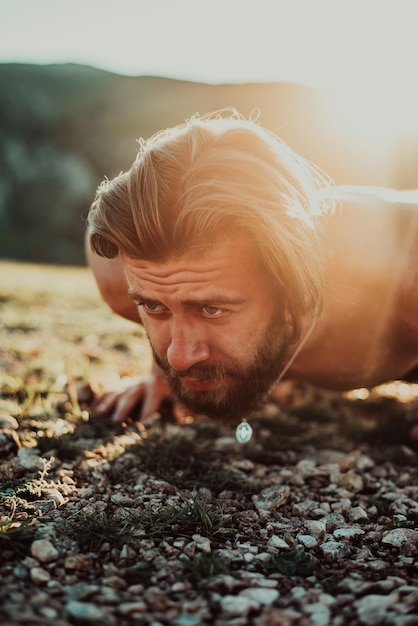 Gespierde moderne man die push-ups doet bovenop een berg in de natuur.