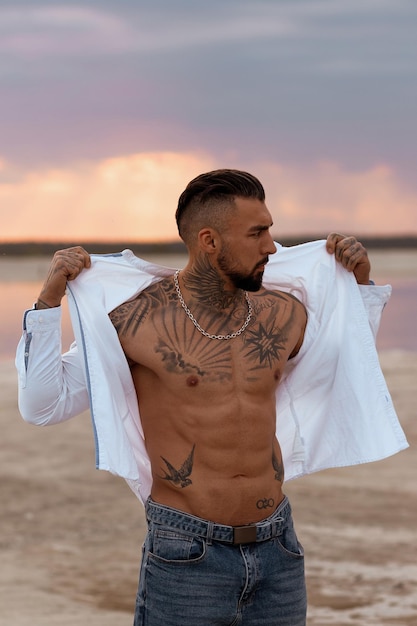 Gespierde sexy jonge man opstijgen t-shirt op leeg wit zandstrand en turquoise oceaan