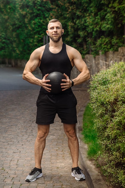 Gespierde sportman die buiten poseert met een fitnessgewichtbal