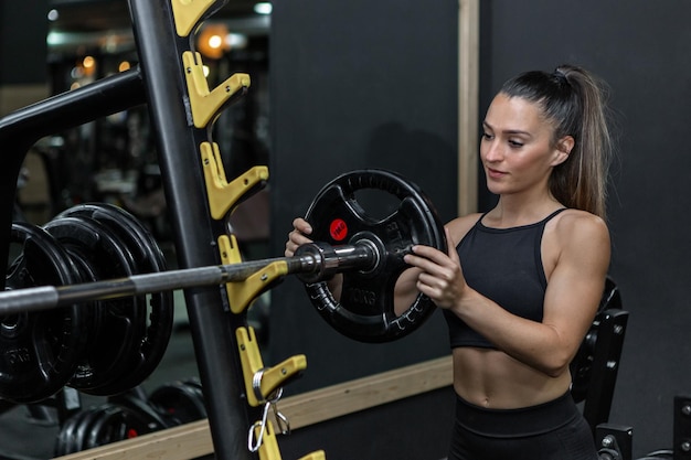 Gespierde sportvrouw die gewichtsplaat op barbell in gymnastiek zet