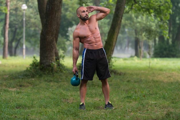 Gespierde volwassen blanke man doet een oefening buitenshuis met kettlebell