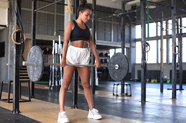 Gespierde vrouw trainen in de sportschool doen oefeningen met barbell op biceps.