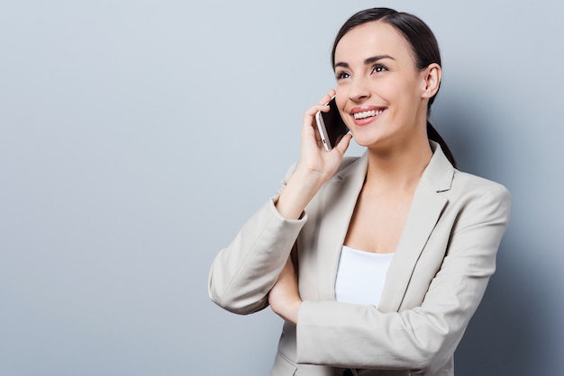 Gesprek met plezier. Mooie jonge zakenvrouwen praten op de mobiele telefoon en glimlachen terwijl ze tegen een grijze achtergrond staan