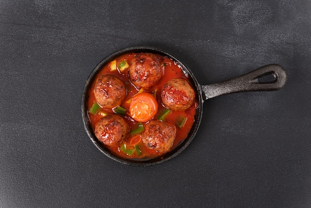 Gestoofde gehaktballetjes in tomatensaus in een pan op een donkere tafel.