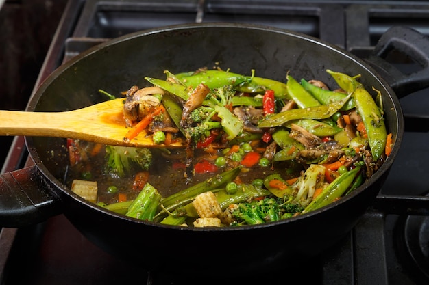 Gestoofde groenten met champignons en broccoli in een koekenpan met een houten spatel