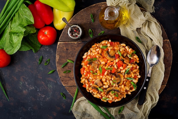 Gestoofde witte bonen met champignons en tomaten met pikante saus in een zwarte kom. Bovenaanzicht. Plat leggen