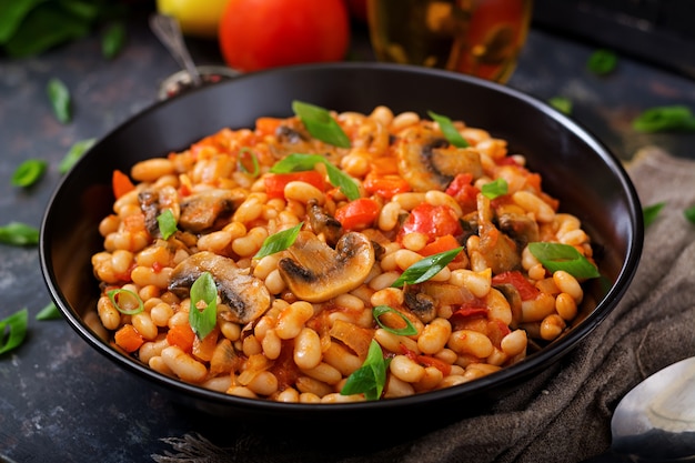 Gestoofde witte bonen met champignons en tomaten met pikante saus in een zwarte kom.