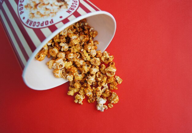 Foto gestreepte kartonnen doos met popcorn op rode muur voor film- en bioscoopliefhebbers.