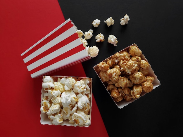 Gestreepte papieren dozen met gezouten en karamel popcorn, zwarte en rode achtergrond, bovenaanzicht.