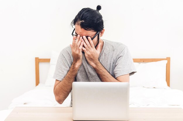 Foto gestresseerde man met laptop op tafel zit tegen een witte achtergrond.