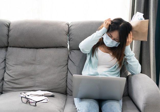 Gestresste Aziatische vrouw zit op de bank, houdt een brief vast, slecht vreselijk negatief nieuws ontslagaankondiging of financiële problemen schuldkennisgeving van de bank tijdens de pandemie van het coronavirus.