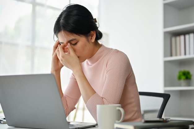 Gestresste aziatische zakenvrouw die last heeft van hoofdpijn terwijl ze zich zorgen maakt over haar werk