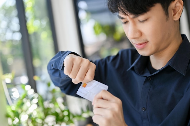 Gestresste en boze jonge Aziatische man die zijn creditcard breekt en zijn creditcard vernietigt