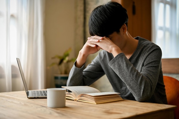 Gestresste en depressieve jonge Aziatische man leest een boek in de coffeeshop en bereidt zich voor op het examen