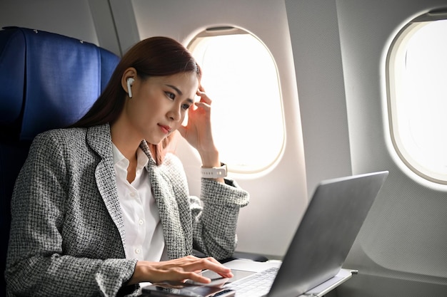 Gestresste en serieuze Aziatische zakenvrouw die haar zakelijke taak uitvoert met behulp van laptop tijdens de vlucht