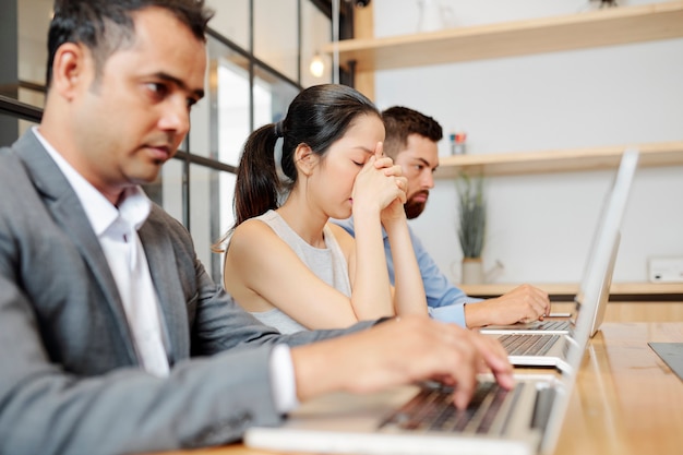 Gestresste, gefrustreerde, bijna huilende jonge zakenvrouw die voor een geopend laptopnest zit voor haar collega's