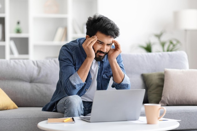 Gestresste Indiase man met hoofdpijn terwijl hij thuis aan een laptop werkt
