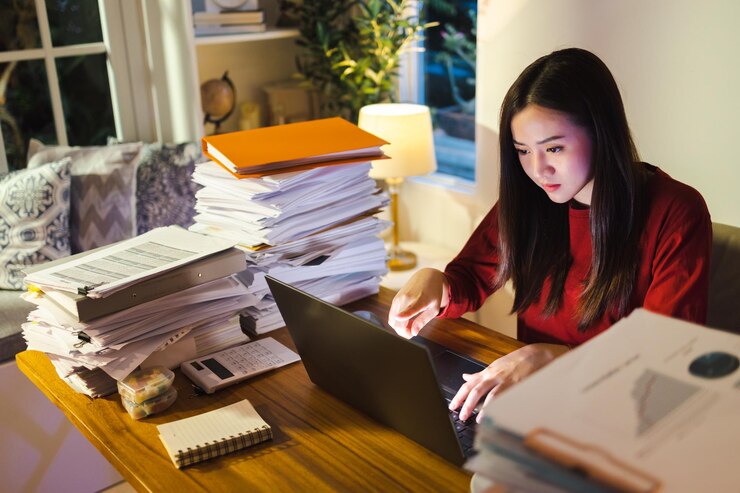 Gestresste jonge vrouw die op een bureau zit, werkt overuren en doet een deadlineproject in de late tijd