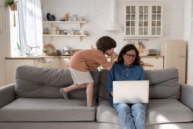 Gestresste jonge vrouw werkt thuis op laptop moe van hyperactief ongehoorzaam klein kind