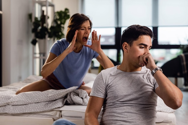 Gestresste man die aan relatieproblemen denkt terwijl zijn vriendin tegen hem schreeuwt in de slaapkamer