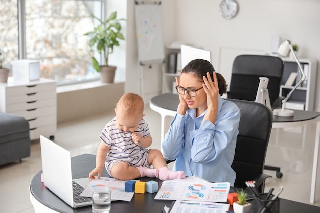 Gestresste moeder met haar baby aan het werk op kantoor