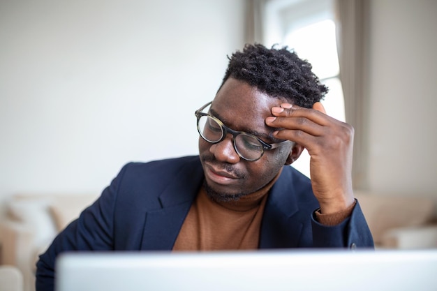 Gestresste vermoeide Afro-Amerikaanse man die tempels aanraakt die lijden aan hoofdpijn na lange uren werken, overwerkte overweldigd zakenman die aan het bureau zit en zich onwel voelt