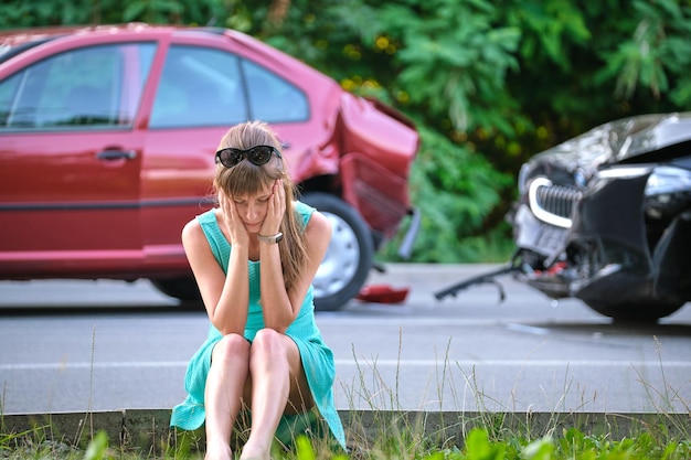Gestresste vrouw die aan de straatkant zit, geschokt na auto-ongeluk Verkeersveiligheid en verzekeringsconcept