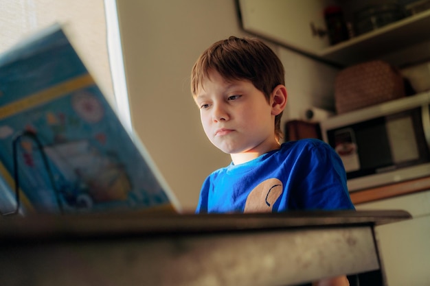 Foto gestrest wanhopige jongen die thuis huiswerk doet aan het bureau bij het raam