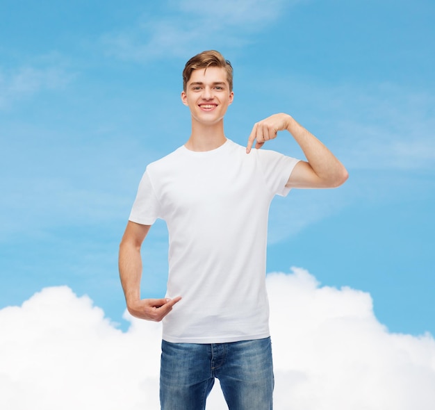 gesture, advertising, dream and people concept - smiling young man in blank white t-shirt pointing fingers on himself over blue sky background