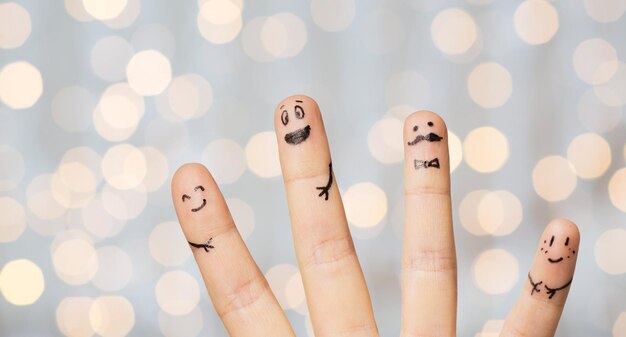 Foto concetto di gesto, famiglia, persone e parti del corpo - primo piano di quattro dita con faccine sorridenti sullo sfondo delle luci delle vacanze