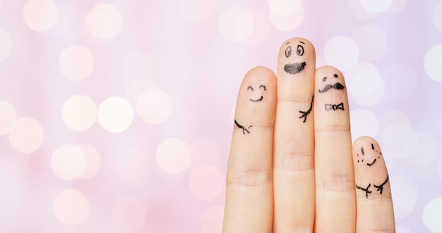 gesture, family, people and body parts concept - close up of four fingers with smiley faces over pink holidays lights background
