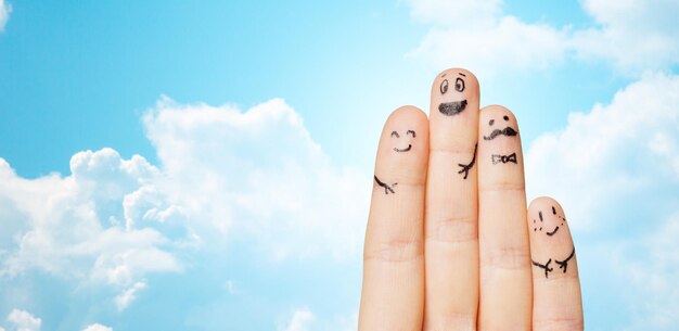 Gesture, family, people and body parts concept - close up of two hands showing fingers with smiley faces over blue sky and clouds background