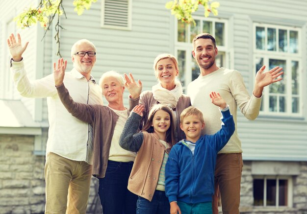 gesture, happiness, generation, home and people concept - happy family waving hands in front of house outdoors