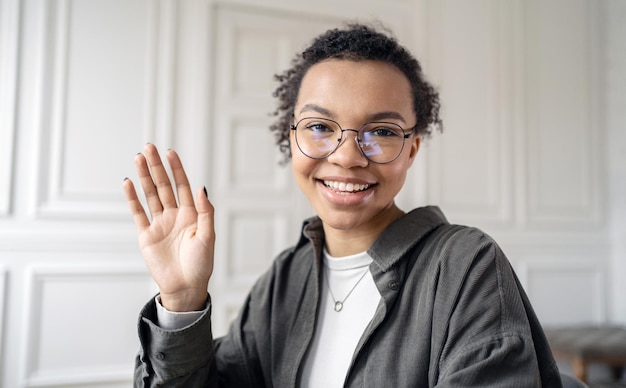 オフィスでオンラインで働く眼鏡の女性とジェスチャーこんにちはビデオ通話フリーランサー