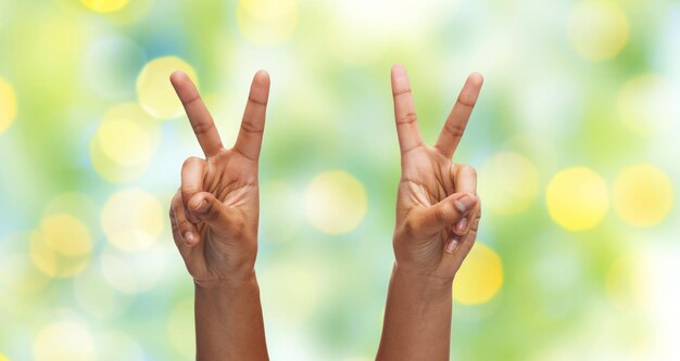 gesture, people and body parts concept - african woman two hands showing victory or peace over blue sky and clouds background