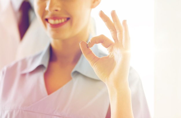 gesture, people and medicine concept - close up of happy female doctor or nurse showing ok hand at hospital