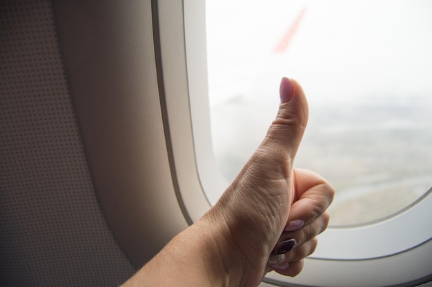 Photo gesture thumb up ok sign womans hand on the background of the window on the plane