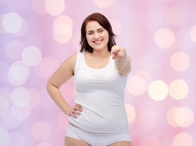 Gesture, weight loss and people concept - smiling young plus size woman in underwear showing over pink holidays lights background