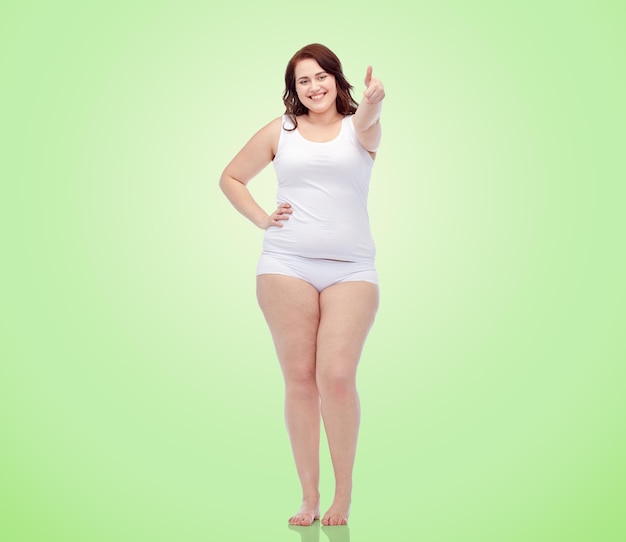 Photo gesture, weight loss and people concept - smiling young plus size woman in underwear showing thumbs up over green natural background