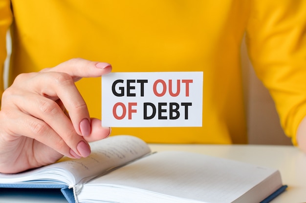 Get out of debt is written on a white business card. a woman's hand holds a white paper card. business and advertising concept. defocus