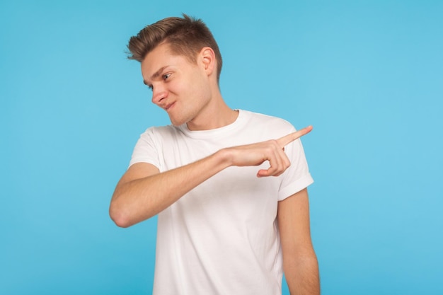 Get out. Portrait of angry guy in white t-shirt dissatisfied with behavior pointing way out, asking to leave him after break up, feeling betrayed. indoor studio shoot isolated on blue background