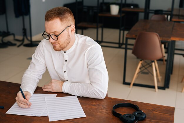 Getalenteerde jonge componist met een stijlvolle bril die muzieknoten schrijft met pen op bladmuziek