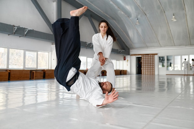 Getalenteerde studente gooit aikido-leraar op de vloer tijdens sparring- en zelfverdedigingstraining in de sportschool