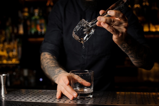 Getatoeëerde barman die een ijsblokje in een cocktailglas zet