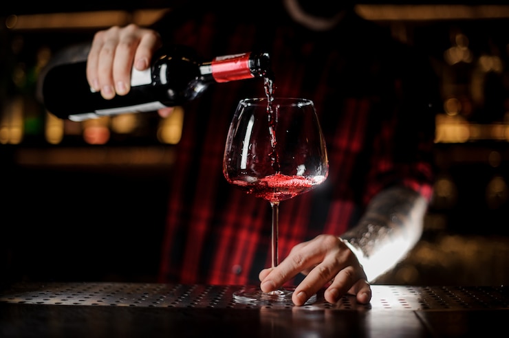 Foto getatoeëerde barman die rode wijn in het burgunya-glas giet