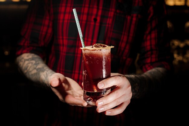 Getatoeëerde barman met een glas koude, verse, sappige bessen alcoholische cocktail met een rietje