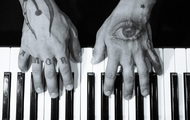 Foto getatoeëerde handen op het toetsenbord van een piano op donkere achtergrond