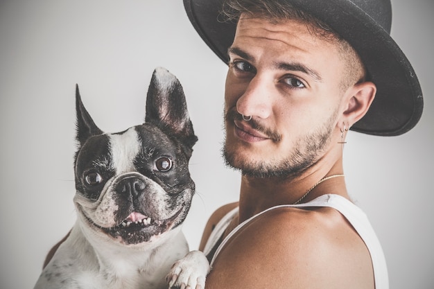 Getatoeëerde jongen met piercings met Franse Bulldog hond in zijn armen op witte achtergrond