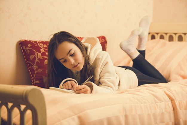 Getinte afbeelding van een mooi tienermeisje dat op bed ligt met haar privédagboek
